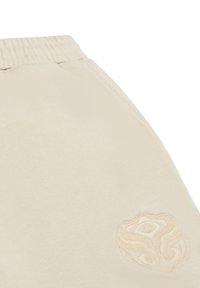 Beige joggers van zachte stof, met een elastische tailleband en een geborduurd logo op het bovenbeen. Gladde textuur, relaxte pasvorm.