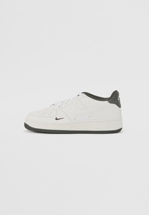 Tenisky Nike Air Force 1 s bielymi koženými vrchnákmi, sivými semišovými akcentmi na päte a textúrovanou gumovou podrážkou.