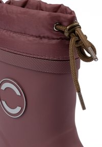 Vízálló bakancs bordó színben, texturált felülettel. Húzózsinóros záródással és egy kerek, ezüst színű logóval az oldalon.