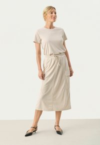 Abito midi beige realizzato in tessuto morbido, con maniche corte, vita elastica, cordoncino e tasca laterale. Abbinato a tacchi neri.