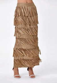 Jupe à franges de couleur beige, composée de franges superposées. Présente une taille ajustée et une longueur maxi. Associée à des sandales à talons blanches.