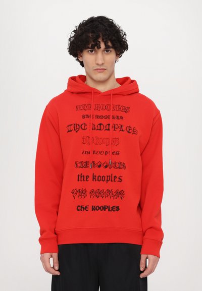 Sweat à capuche rouge avec plusieurs logos en texte noir. Il possède une capuche avec cordon et des poignets côtelés. Le tissu semble doux et décontracté.