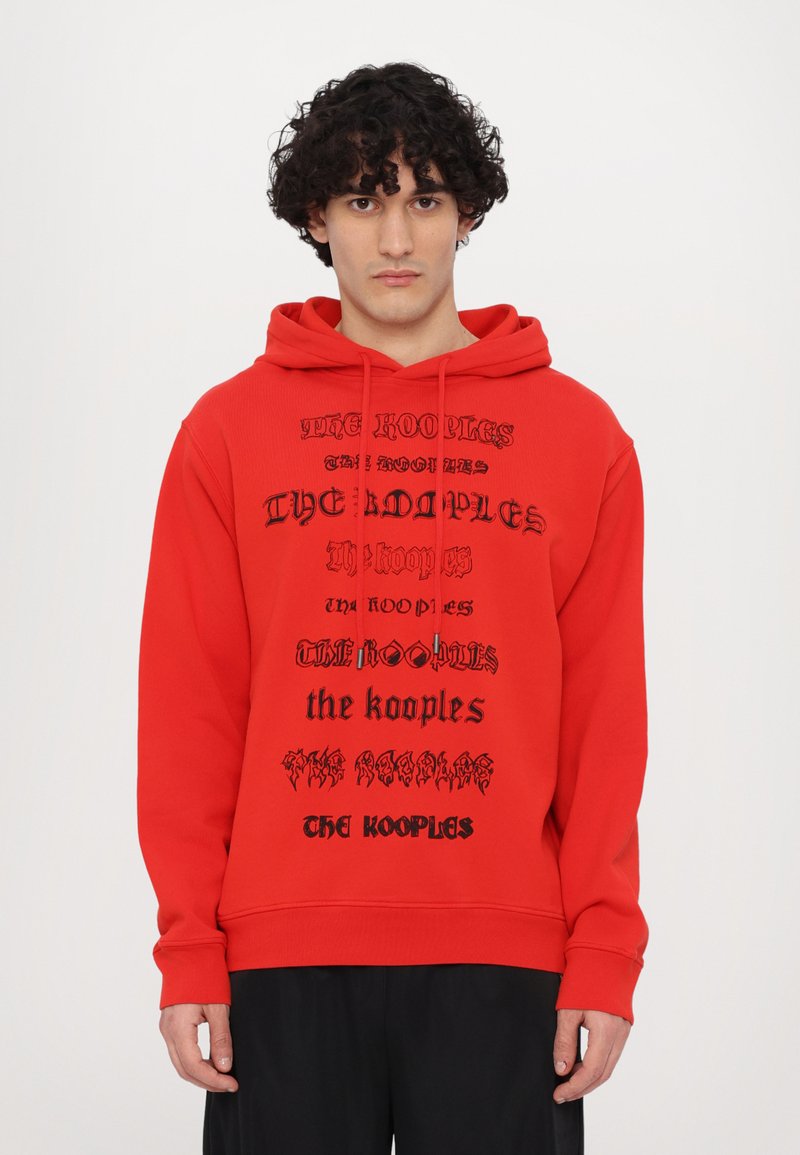 Rode hoodie met meerdere zwarte tekstlogo's. Het heeft een capuchon met trekkoord en ribbelboorden. De stof lijkt glad en casual.