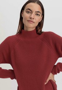 Maglione ribbed color marsala con collo alto, spalle scese e maniche lunghe. Presenta un design a maglia texture e una vestibilità rilassata.