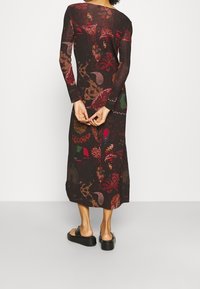 Robe longue noire avec des motifs floraux et abstraits colorés, manches longues, et coupe droite, accompagnée de sandales à plateforme noires.