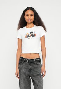 Λευκό κοντομάνικο μπλουζάκι με τυπωτό σχέδιο δύο κινούμενων χαρακτήρων σε χρώμα, με στρογγυλή λαιμόκοψη και κοντά μανίκια. Μαύρο τζιν με ζώνη.