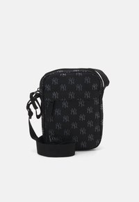 Svart crossbody veske med et mønstret NY-logo. Har glidelås, justerbar stropp og teksturert stoff. Kompakt rektangulær form.