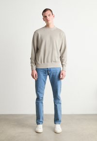 Lys grå hettegenser med ribbestrikkede mansjetter og hem, parret med blå jeans og hvite sneakers. Enkelt design, ensfarget, avslappet passform.