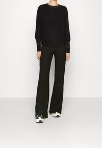 Suéter negro de punto con cuello redondo y detalles de tachuelas en las mangas, combinado con pantalones amplios negros texturizados. Zapatillas blancas y negras.
