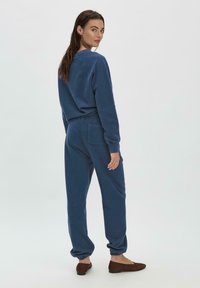 Sudadera de algodón azul y joggers a juego con piernas acanaladas. El conjunto cuenta con un bolsillo trasero en los pantalones y un diseño de corte relajado.