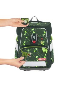 Grüner Rucksack mit geometrischem Muster, einem zentralen Verschluss und mehreren anbringbaren Dinosaurier-Patches in leuchtenden Farben.