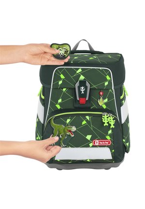 Sac à dos vert avec un motif géométrique, un fermoir central et plusieurs patches amovibles sur le thème des dinosaures dans des couleurs vives.