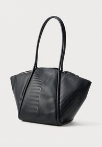 Svart handväska med texturerade vertikala ränder, strukturerad trapezform, och två långa handtag som sträcker sig ovanför väskans öppning med dragkedjestängning.