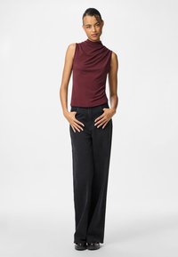 Top sin mangas burdeos con tela drapeada, combinado con pantalones de pierna ancha negros de tiro alto. Textura suave y diseño discreto.