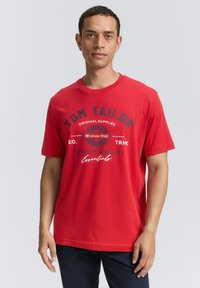 Rød bomulds t-shirt med rund hals, korte ærmer og et grafisk print med teksten "Tom Tailor" og "Premium Quality" i mørke farver.