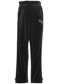 Svarta flådiga joggers med elastisk midja, med ett vitt hjärta och logotryck på vänster lår samt dragkedjor vid anklarna.