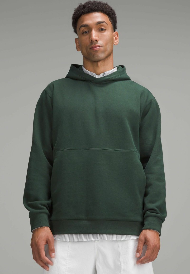 Groene hoodie gemaakt van zachte stof, met een voorzak en geribde manchetten. Draag over een gestreepte overhemd met kraag.