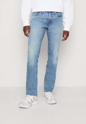 Lichtblauwe denimjeans met een rechte pasvorm, met subtiele vervaging en een klassieke five-pocketontwerp, gecombineerd met witte sneakers.