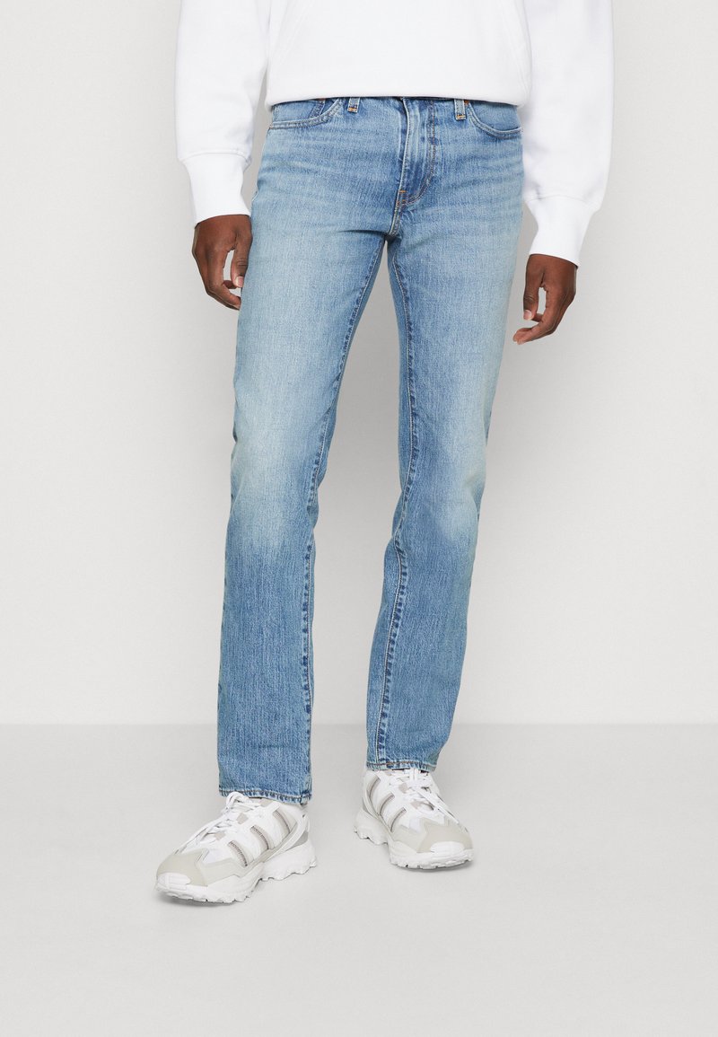 Lyseblå denim jeans med rett benpassform, med subtile falminger og klassisk fem-lommers design, kombinert med hvite sneakers.