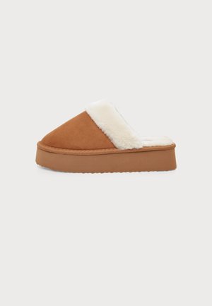 Brūnas slip-on platformas čības ar baltu mīkstu kažokādu oderi un biezu zoli uz gaiša vienveidīga fona.