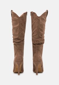 Bottes montantes en daim marron avec un bout pointu et un talon haut fin. Texture froncée, fermeture éclair arrière et détail de bord supérieur festonné.