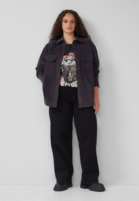 Donkerpaarse corduroy overhemdjasje met twee voorkwasten, gedragen over een graphic T-shirt met een tijgerprint, in combinatie met zwarte wijde broek.