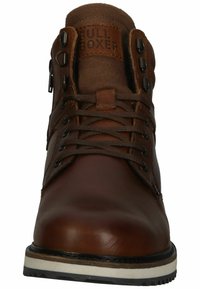 Bota de cuero marrón con cordones, cuello acolchado, ojales de metal y suela de goma blanca robusta. Parche con el logo en la lengüeta.
