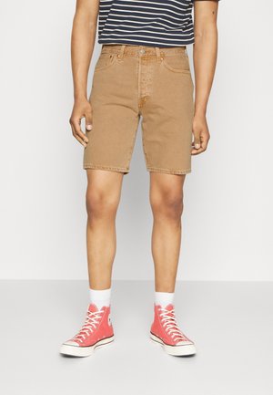 Brązowe szorty z denimu o prostym kroju, z przednimi kieszeniami i przeszywanym wykończeniem. W połączeniu z czerwonymi tenisówkami z płótna i białymi skarpetkami.