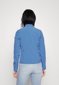 Blue, fitted jacket with a high collar, long sleeves, and button cuffs; made of smooth fabric with a minimalist design and logo detail.