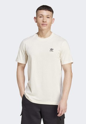 T-shirt in cotone color crema con maniche corte, colletto rotondo e un piccolo logo Adidas nero sul lato sinistro del petto. Design a vestibilità casual.