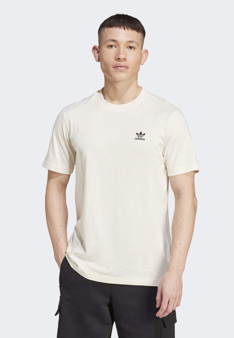 Krémové bavlněné tričko s krátkými rukávy, kulatým výstřihem a malým černým logem Adidas na levé části hrudi. Design v uvolněn�ém střihu.