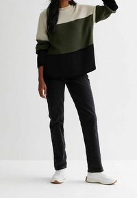 Maglione lavorato a maglia con righe orizzontali color crema, verde oliva e nero, abbinato a jeans neri e scarpe da ginnastica bianche. Tessuto testurizzato, vestibilità ampia.