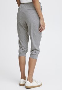 Grå capribukser med en myk tekstur, elastisk midje og oppbrettede hem, kombinert med hvite joggesko og med to baklommer.