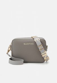 Grå läderväska med axelrem, guldfärgad logotyp, avtagbar rem med bokstavsdetaljer, dragkedjestängning och rektangulär form.