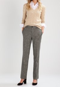 Un pull en maille beige porté par-dessus une chemise blanche à col, associé à un pantalon à carreaux gris et des escarpins noirs. La tenue présente une coupe décontractée.