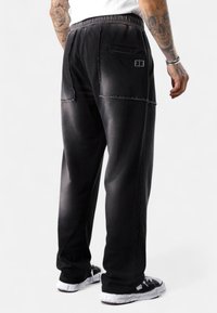 Schwarze Jogginghose mit texturiertem Finish, enthält gestickte Akzente, seitliche Taschen und einen elastischen Bund. Eng an den Knöcheln.