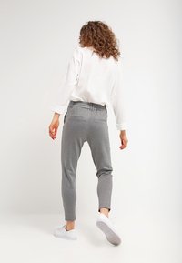 Graue Jogginghosen mit einem elastischen Bund, ausgestattet mit Seitentaschen und einer schlanken, schmalen Passform. Kombiniert mit einem lockeren weißen Shirt und weißen Schuhen.