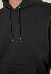 Svart hoodie i bomullsmaterial blandning, med en framficka, silverfärgade snören och ett mjukt, strukturerat tyg.