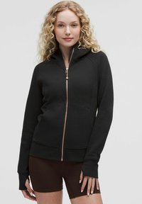 Black zip-up hoodie made from a soft fabric with a fitted design. Features a hood, raglan sleeves, and copper-colored zipper details.