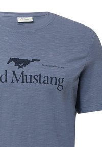 Niebieska koszulka z czarną grafiką biegającego mustanga oraz napisem "Mustangers zawsze wygrywają." i "d Mustang" z przodu.