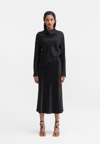 Sorte kjole i glat stof med draperet halsudskæring og lange ærmer; har en midi-længde og minimalistisk design. Båret med sandaler med stropper.