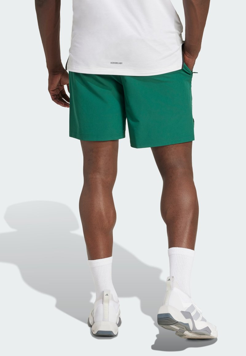 Pantalones cortos deportivos verdes con una textura suave, bolsillos laterales y un ajuste relajado. Combinados con calcetines blancos y zapatos de color claro.