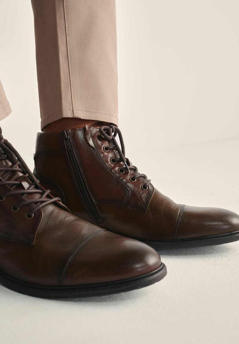 Brązowe skórzane botki za kostkę z okrągłymi noskami, z sznurowaniem i zamkiem błyskawicznym, o gładkiej fakturze i subtelnych detalach w postaci szwów.