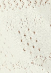 Tissu tricoté avec une base blanche et des motifs de points et de diamants marron. Texture douce avec des détails de fibres visibles et un léger éclat.