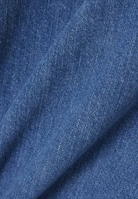 Gros plan sur un tissu en denim bleu montrant un tissage texturé et des plis subtils.