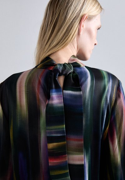 Blusa traslucida in tessuto scuro con strisce verticali in verde, viola e rosso. Dettaglio al collo annodato con design della schiena scoperta.
