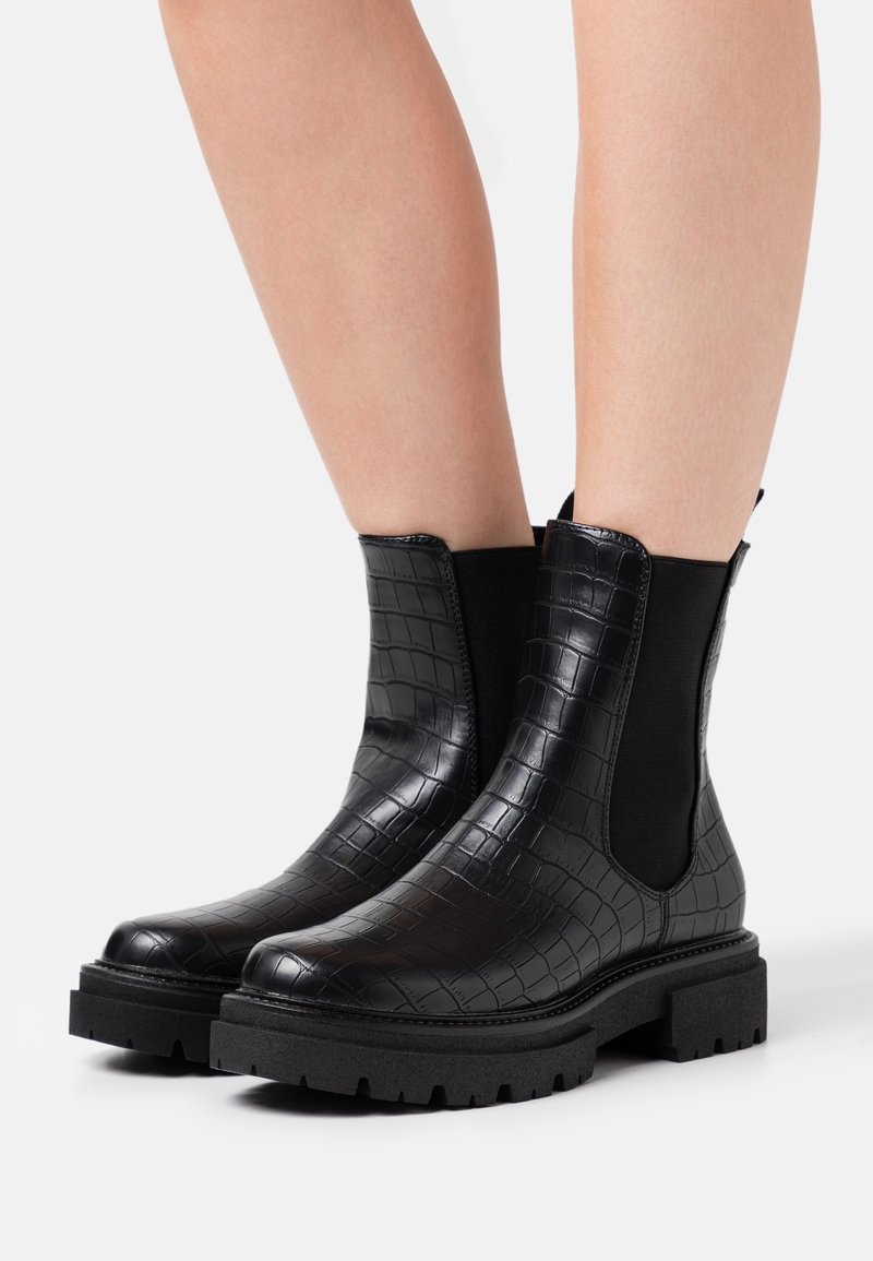 Bottes noires à la cheville avec une texture peau de crocodile, des panneaux latéraux élastiques et des semelles en caoutchouc épaisses. Finition lisse avec des languettes au talon.