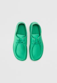 Pantofi din piele verde, cu vârf rotund, textură netedă și design minimalist. Caracteristici include accente cu șireturi și o talpă flexibilă.
