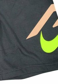 Schwarze Shorts aus Stoff mit einem großen neongrünen Nike-Logo und einem beigen geometrischen Design. Glatte Textur mit gesteppten Säumen.