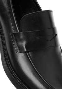 Mocassins en cuir noir à texture lisse, avec une large bride et des coutures discrètes le long de la semelle, mettant en valeur un design classique.